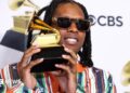 Lil Durk wearing sunglasses and a multi-coloured suit, and holding up the gold gramophone-shaped Grammy Award