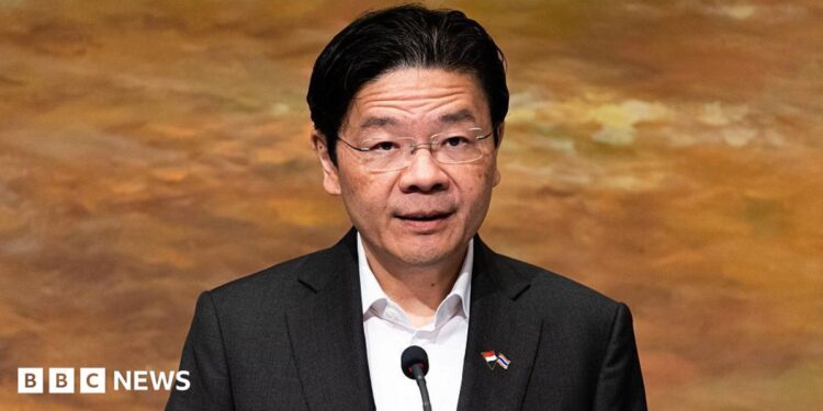 Lawrence Wong in a black suit and white shirt addresses a crowd on a podium