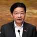 Lawrence Wong in a black suit and white shirt addresses a crowd on a podium