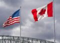 An American and Canadian flag flutter on poles over a bridge.