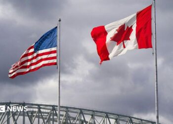 An American and Canadian flag flutter on poles over a bridge.