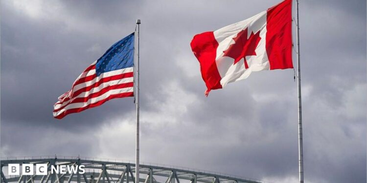 An American and Canadian flag flutter on poles over a bridge.