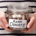 A shot of someone's torso, in a black and white striped top, holding a glass jar with coins in it. On the front is a label that reads: Please donate.