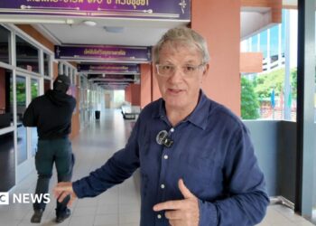 BBC correspondent Jonathan Head and a man dressed in black standing in a school corridor in Bangkok