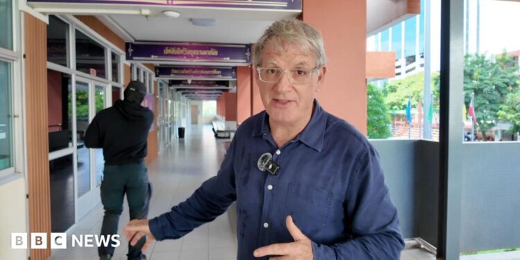 BBC correspondent Jonathan Head and a man dressed in black standing in a school corridor in Bangkok
