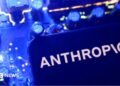 A smartphone display showing the Anthropic logo in black letters on an all-white background, laid on a laptop keyboard lit in pink and purple