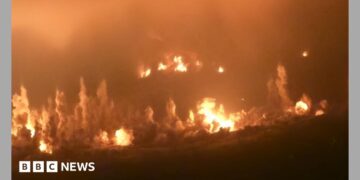 Huge flames and pillars of smoke rise from the ground in a night-time picture