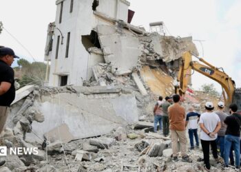 Men look at an excavator working at the site of an Israeli strike in Arab Salim, southern Lebanon