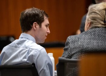 Tyler Robinson and Kathryn Nester sitting at a table with their backs to the camera in a courtroom setting.