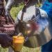 A close-up of someone's hand holding a large stove-top kettle and pouring a brown milky liquid into a yellow cup being held by someone else.