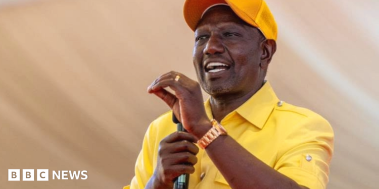 William Ruto in a yellow shirt and cap gestures with his hand as he makes a speech holding a microphone in his other hand.