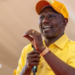 William Ruto in a yellow shirt and cap gestures with his hand as he makes a speech holding a microphone in his other hand.