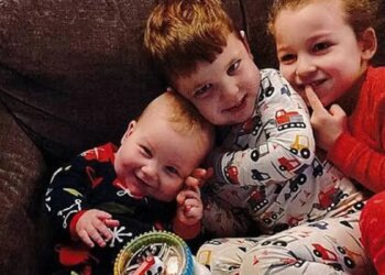 Three young Clancy children in pajamas sit together on a couch, the smiling baby resting against his older brother, with their sister beside them.