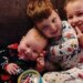 Three young Clancy children in pajamas sit together on a couch, the smiling baby resting against his older brother, with their sister beside them.
