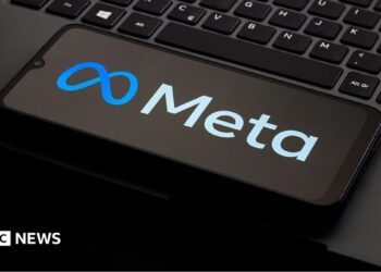 A photo of a phone kept on a laptop keyboard. The phone is displaying the logo of the company Meta