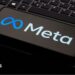 A photo of a phone kept on a laptop keyboard. The phone is displaying the logo of the company Meta