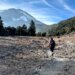 A rescuer hikes along rough terrain and rocks toward Mount Shasta