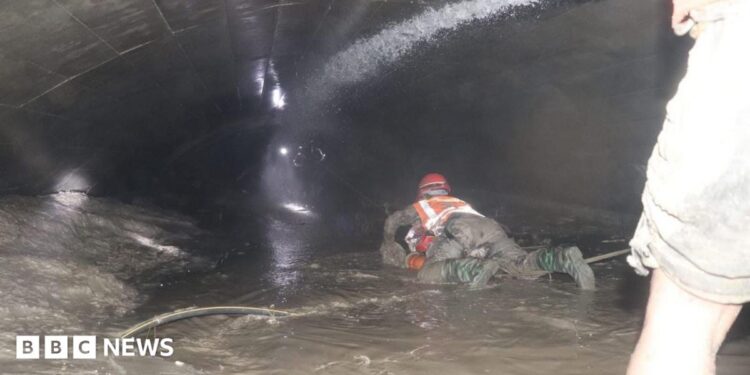 Nepalese rescuers wading through puddles of water in the Trishuli 3A tunnel