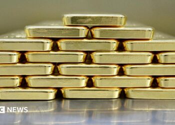 Gold bars are neatly stacked on top of each other to form a pyramid shape.