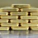 Gold bars are neatly stacked on top of each other to form a pyramid shape.