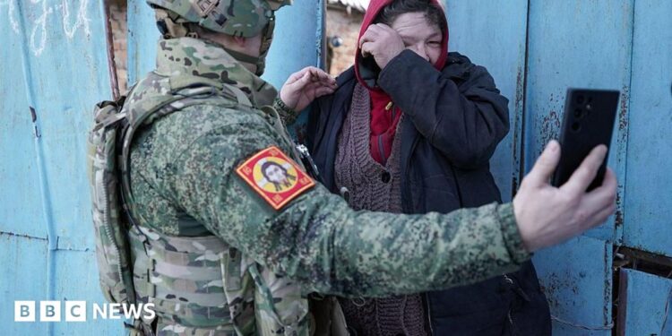 Local resident watches a video message of her relative on the smartphone of a Chechen Akhmat battalion fighter in the village of Kazachya Loknya in March 2025