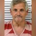 Booking photo of John Herb Hayes III, a gray-haired man wearing a red-and-pink striped shirt in front of a height chart.
