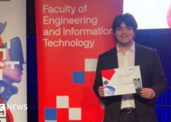 A young man in a suit holding up a certificate and standing in front of signs, one titled UTS Tech Festival and another Faculty of Engineering and Information Technology