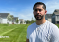 Gerald Bourguet, a white man standing in a field of a manicured lawn. He is wearing a white shirt and crucifix chain. There are homes in the background that are blurred.