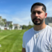 Gerald Bourguet, a white man standing in a field of a manicured lawn. He is wearing a white shirt and crucifix chain. There are homes in the background that are blurred.
