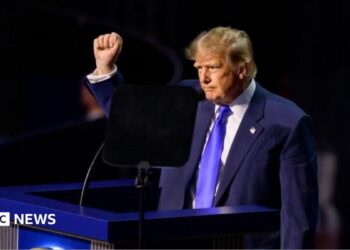 Trump wearing a blue suit and tie and white shirt opens his arms as he addresses the convention in Dallas