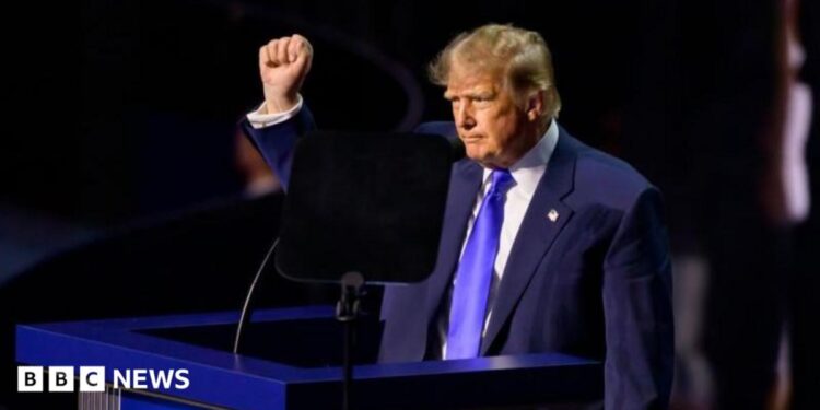 Trump wearing a blue suit and tie and white shirt opens his arms as he addresses the convention in Dallas