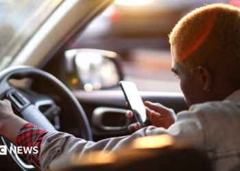 An Uber driver looking at his phone as he waits for his customer