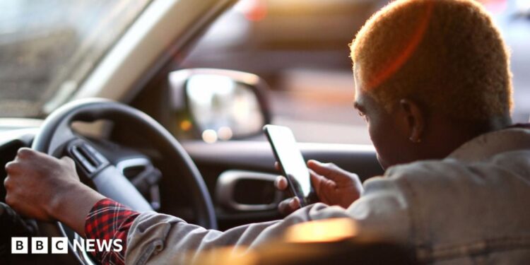 An Uber driver looking at his phone as he waits for his customer