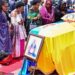 Family members and mourners attend a ceremony to receive the coffin with the body of King Oyo Nyimba Kabamba Iguru Rukidi IV at Entebbe airport. The casket is draped in the Tooro kingdom flag and the Ugandan flag. A portrait of the monarch has been place at the front of the coffin and woman in a black shawl is kneeling before it.