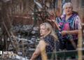 Two middle-aged women stare into the distance amid the rubble from a Russian attack