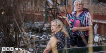 Two middle-aged women stare into the distance amid the rubble from a Russian attack