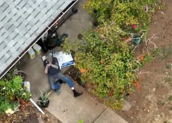 A suspect aims a rifle skyward outside a rural house