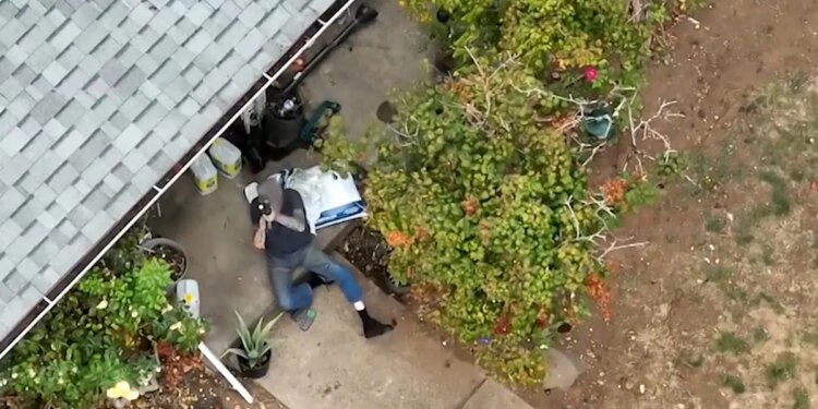 A suspect aims a rifle skyward outside a rural house