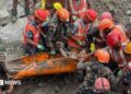 A group of rescuers holding a man on an orange stretcher.