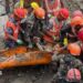 A group of rescuers holding a man on an orange stretcher.