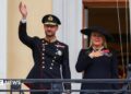 King Haakon waves to the crowd from the balcony of the royal palace, as Queen Mette-Marit stands next to him
