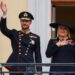 King Haakon waves to the crowd from the balcony of the royal palace, as Queen Mette-Marit stands next to him
