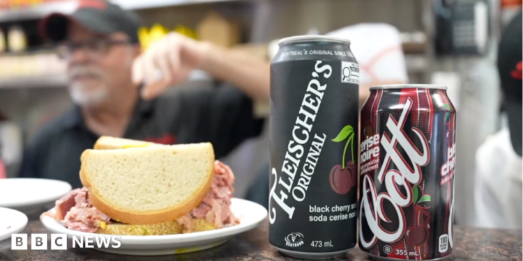 A sandwich and two types of cherry cola on a countertop in a deli.