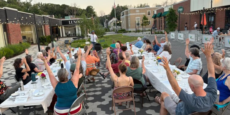 Community members raise their arms during a gratitude poem at a supper in Westbrook, Maine, in July 2025 [Courtesy of Community Plate]