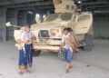 An armed man walks next to an armoured vehicle, in Mocha
