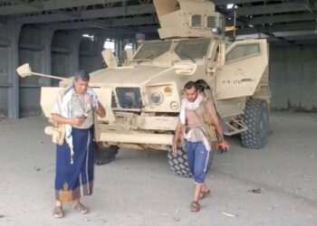 An armed man walks next to an armoured vehicle, in Mocha